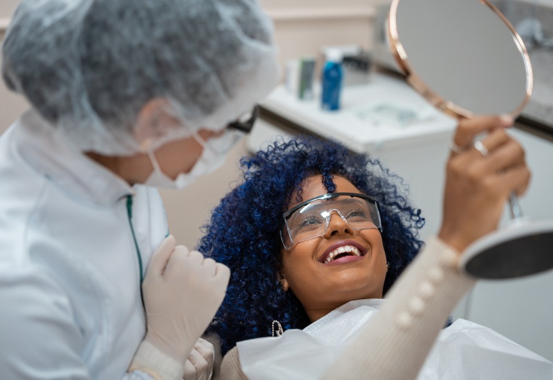 A Smiling woman admires her smile in a mirror after cosmetic dentistry treatment in Brookfield, WI