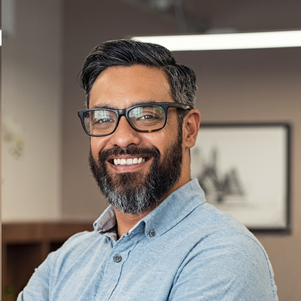 A smiling man with glasses in a blue shirt, representing dental cleaning services in Brookfield, WI