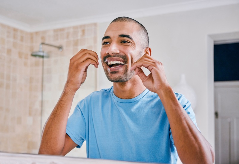 A man smiling while flossing, showing the benefits of dental floss for oral health in Brookfield, WI