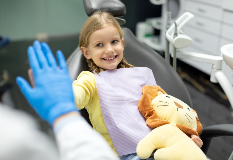 A smiling girl in a clinic with a dentist & a toy promoting oral health habits in Brookfield, WI