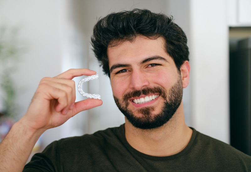 A smiling man holding an clear aligner, promoting orthodontic care in Brookfield, WI
